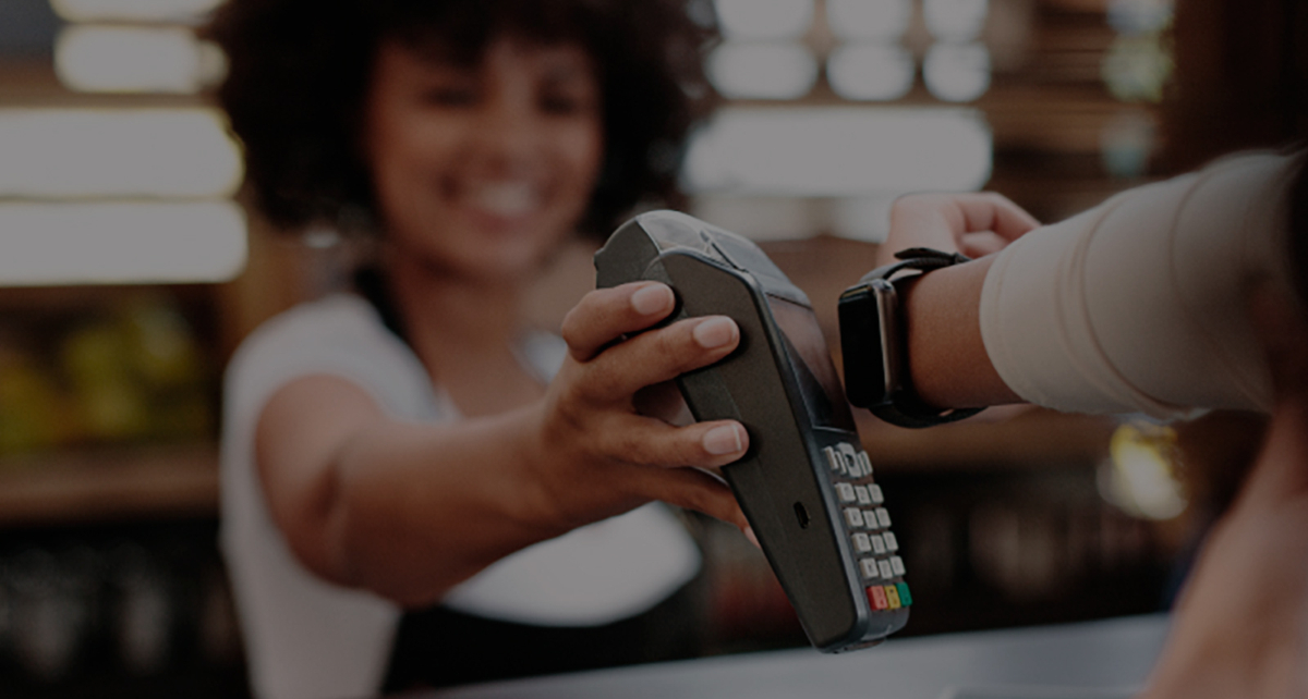 Store clerk holding payment terminal for a woman to tap with her smart watch for payment.